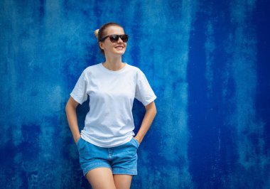 Mavi bir duvarın arka planında beyaz tişört giyen kadın model.