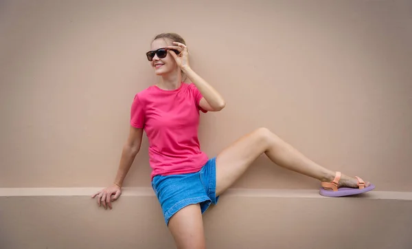 Female model wearing pink blank t-shirt on the background of an sandy wall