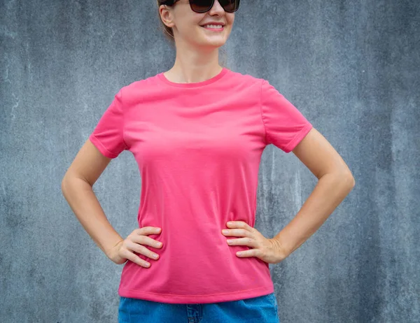 Female model wearing pink blank t-shirt on the background of an gray scratched wall