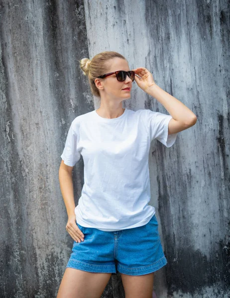 Female model wearing white blank t-shirt on the background of an gray scratched wall