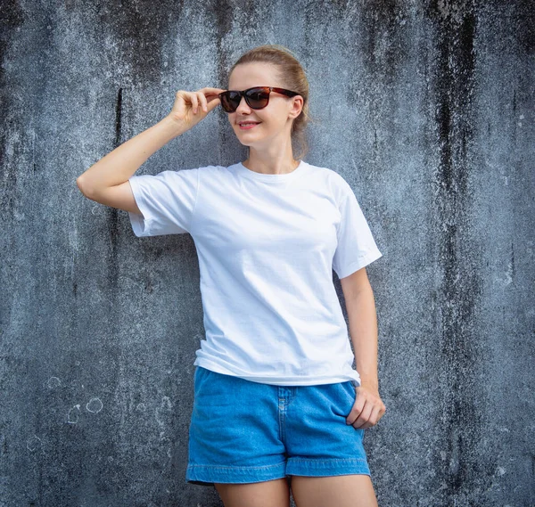 Female model wearing white blank t-shirt on the background of an gray scratched wall