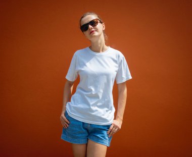 Turuncu bir duvarın arka planında beyaz tişört giyen kadın model.