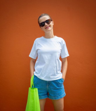 Turuncu bir duvarın arka planında beyaz tişört giyen kadın model.