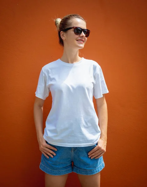 Female model wearing white blank t-shirt on the background of an orange wall