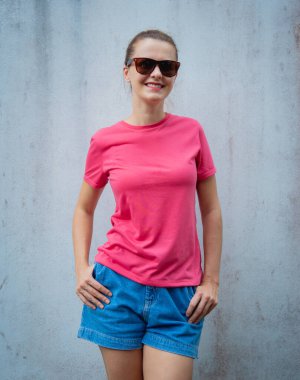 Gri bir duvarın arka planında pembe, boş tişört giyen kadın model.