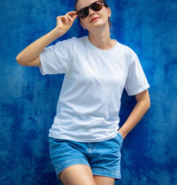 Mavi bir duvarın arka planında beyaz tişört giyen kadın model.