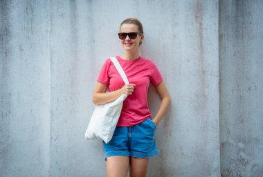 Gri bir duvarın arka planında pembe, boş tişört giyen kadın model.