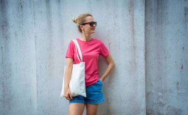 Gri bir duvarın arka planında pembe, boş tişört giyen kadın model.