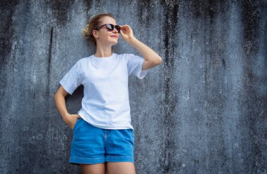 Beyaz beyaz tişört giyen kadın manken arka planda gri bir duvar çiziği var.