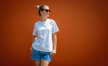 Turuncu bir duvarın arka planında beyaz tişört giyen kadın model.