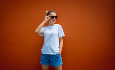 Turuncu bir duvarın arka planında beyaz tişört giyen kadın model.