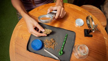 Hippi tarzı kadın büyüteç altında tıbbi marihuananın eklemlerini ve tomurcuklarını inceliyor..