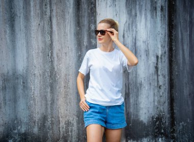 Beyaz beyaz tişört giyen kadın manken arka planda gri bir duvar çiziği var.