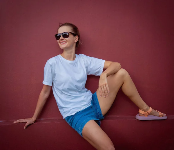 Female model wearing white blank t-shirt on the background of an burgundy wall