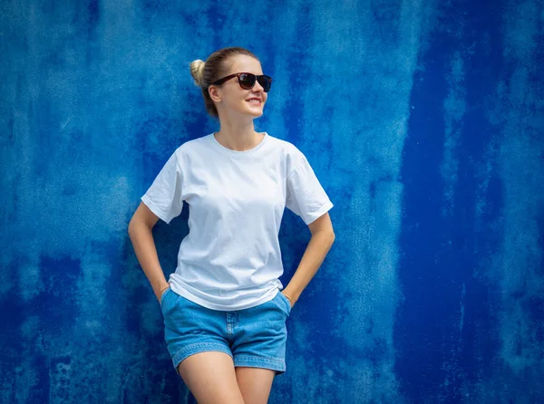 Female model wearing white blank t-shirt on the background of an blue wall