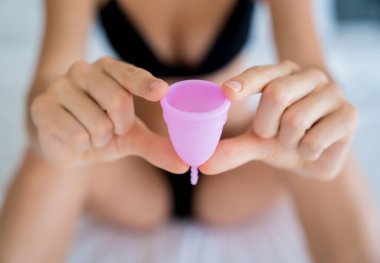 Young beautiful woman at home holding a menstrual cup in her hands.