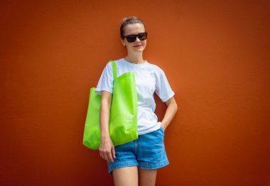 Turuncu bir duvarın arka planında beyaz tişört giyen kadın model.