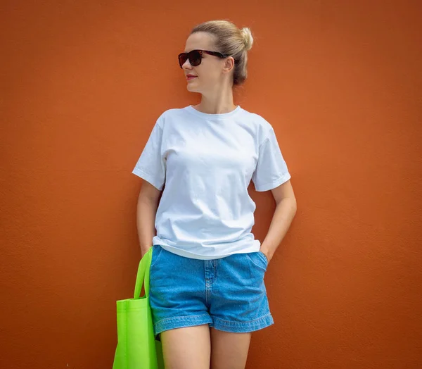 Female model wearing white blank t-shirt on the background of an orange wall
