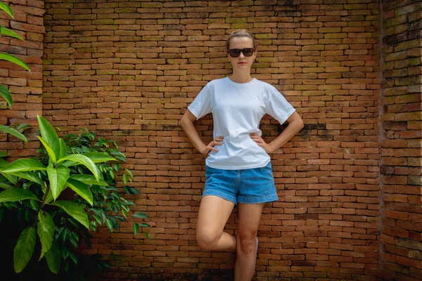 Female model wearing white blank t-shirt on the background of an bricks wall