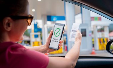Woman using contactless payment by mobile phone with QR code at car filling station.