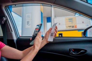 Woman using contactless payment by mobile phone with QR code at car filling station.