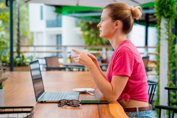 Young woman drinking coffee at the table with notebook in cafe.