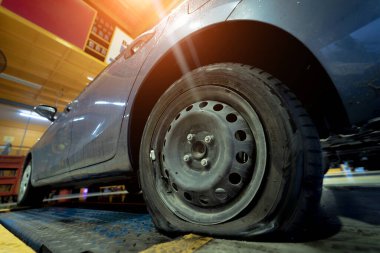 Car with a punctured and broken wheel in a car repair shop.