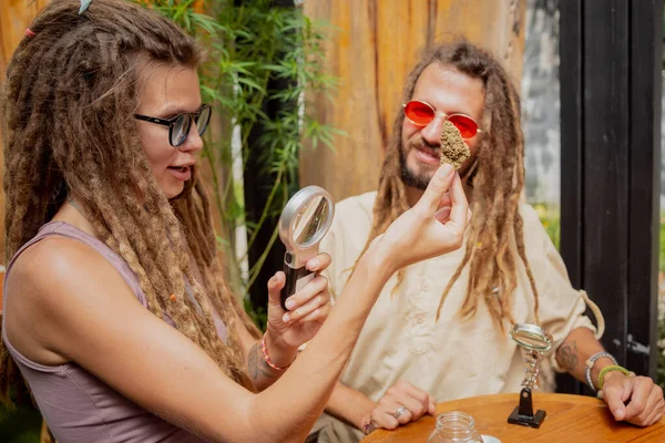 嬉皮风格的夫妇在放大镜下检查医用大麻的接缝和芽 — 图库照片