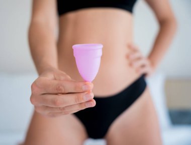 Young beautiful woman at home holding a menstrual cup in her hands.