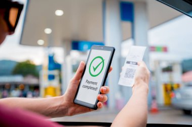 Araç dolum istasyonunda QR kodlu cep telefonuyla ücretsiz ödeme yapan bir kadın..