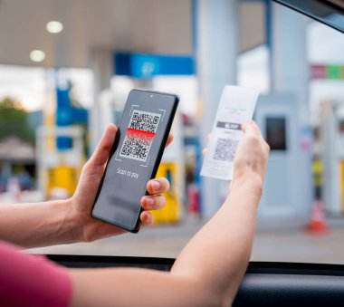 Araç dolum istasyonunda QR kodlu cep telefonuyla ücretsiz ödeme yapan bir kadın..