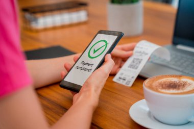 Woman using contactless payment by mobile phone with QR code at cafe.