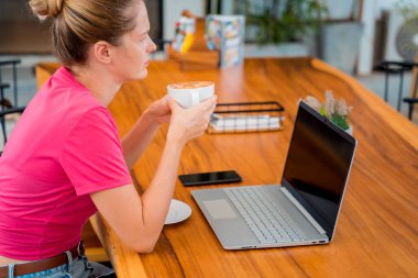 Young woman drinking coffee at the table with notebook in cafe.