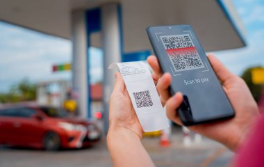 Woman using contactless payment by mobile phone with QR code at car filling station.