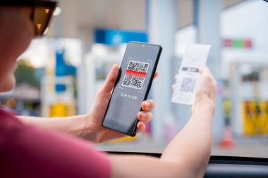 Araç dolum istasyonunda QR kodlu cep telefonuyla ücretsiz ödeme yapan bir kadın..