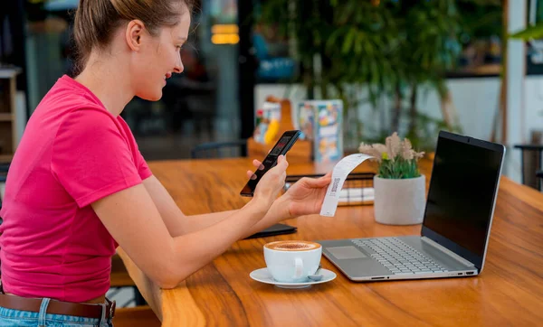 Woman using contactless payment by mobile phone with QR code at cafe.