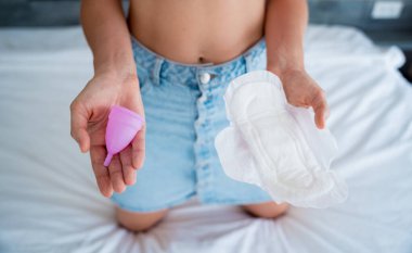 Young woman holding menstrual cup and sanitary pads in her hands.