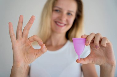 Young beautiful woman at home holding a menstrual cup in her hands.