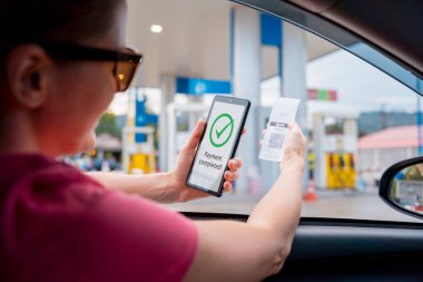 Woman using contactless payment by mobile phone with QR code at car filling station.