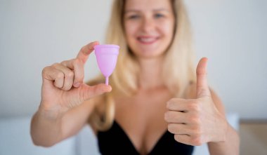 Young beautiful woman at home holding a menstrual cup in her hands.