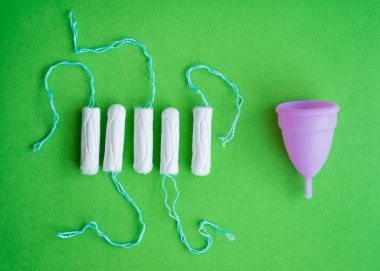 Menstrual cup, tampons on a green background, concept of critical days.