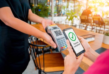 Woman using contactless payment by mobile phone with QR code at cafe.