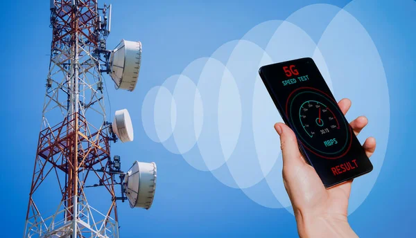 信号を受信する5Gセルタワーの背景に携帯電話を持つ手 — ストック写真