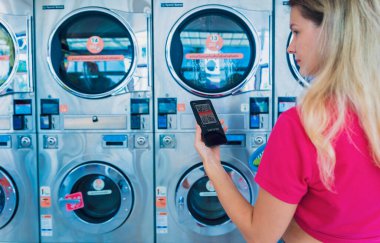 Genç kadın çamaşırhane için telefon ve bankacılık başvurusuyla ödeme yapıyor..