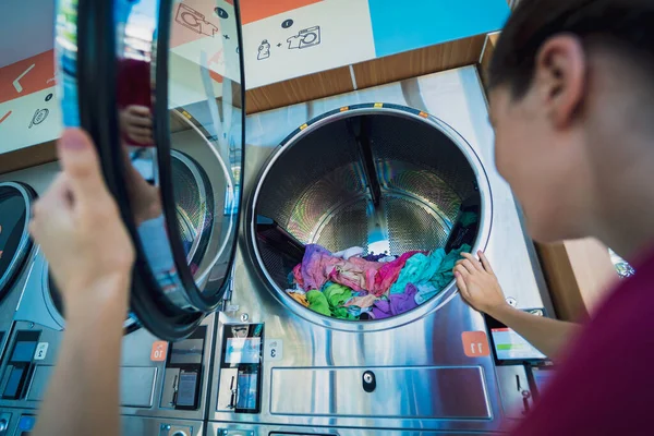 Young beautiful woman washes and dries clothes in the laundry.