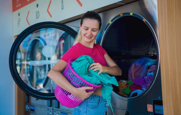 Young beautiful woman washes and dries clothes in the laundry.