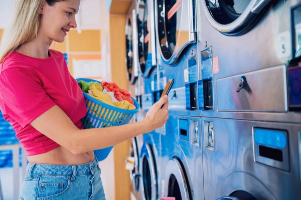 年轻妇女使用电话和银行应用程序支付洗衣服务费用 — 图库照片