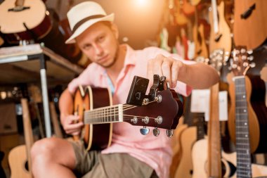 Genç bir müzisyen gitar dükkanında klasik gitar akort ediyor..