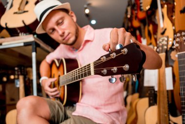 Genç bir müzisyen gitar dükkanında klasik gitar akort ediyor..