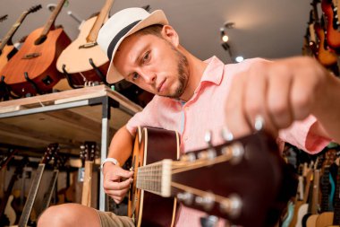 Genç bir müzisyen gitar dükkanında klasik gitar akort ediyor..